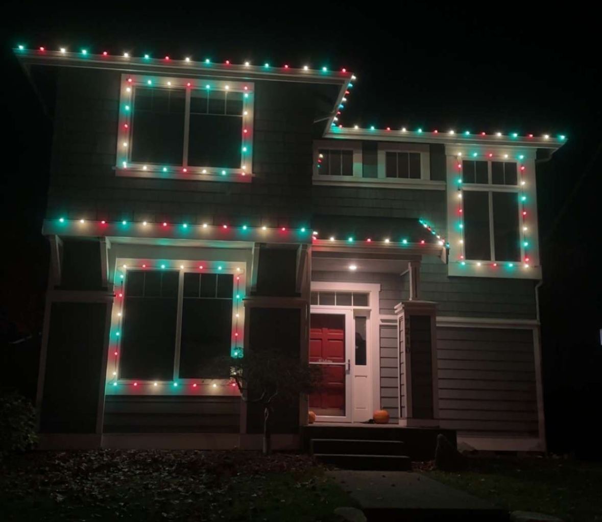 Two-story home with red, teal and white lights on the rooflines and around every window